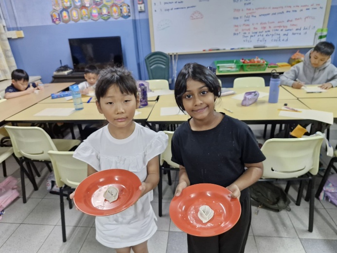 A couple of children holding plates in a classroom

Description automatically generated